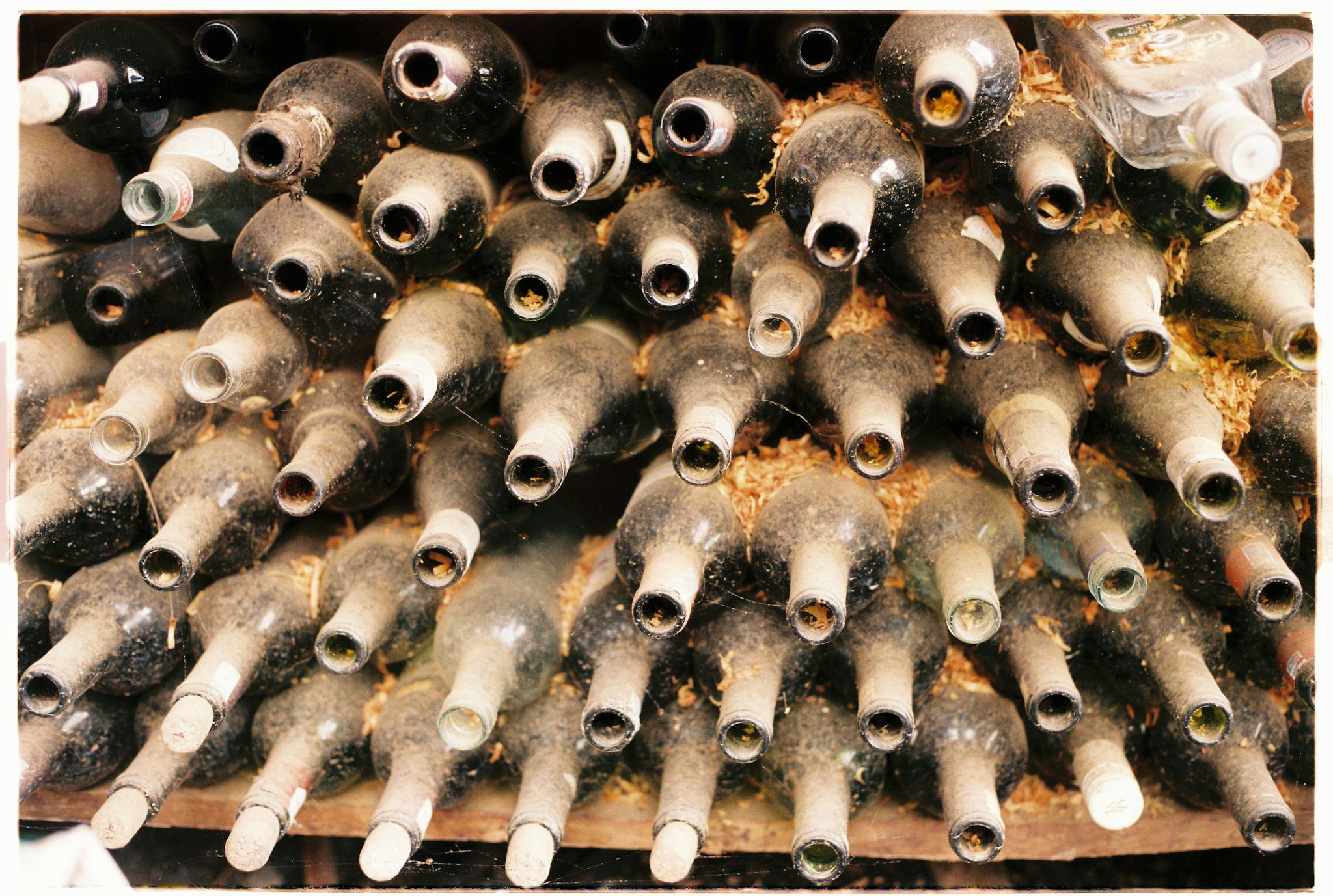 A collection of dusty, empty wine bottles stacked horizontally in an old cellar.