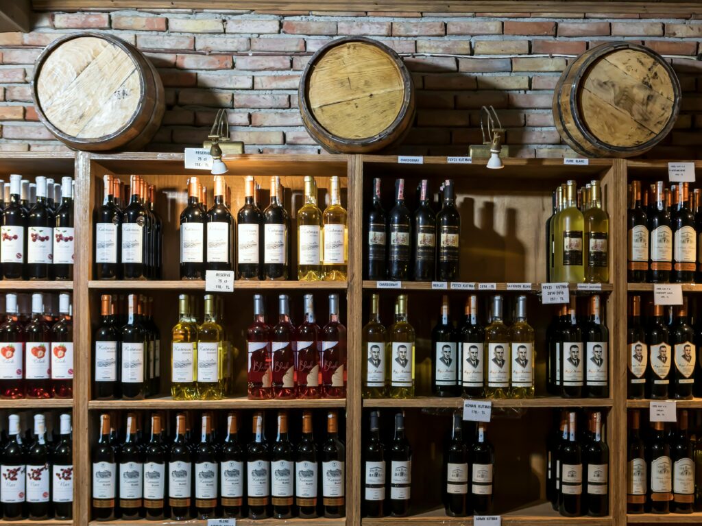 A rustic wine cellar showcasing a variety of wine bottles against a brick wall and wooden barrels.